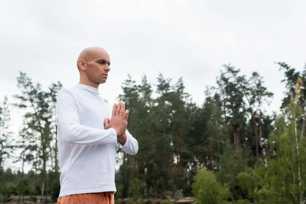 buddhist in white sweatshirt praying in forest